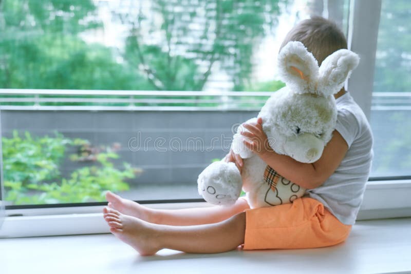 Boy of two years sitting by the window and hugs a toy Bunny. rainy weather, waiting for dad to come home from work royalty free stock images Boy of two years sitting by the window and hugs a toy Bunny. rainy weather, waiting for dad to come home from work royalty free stock images