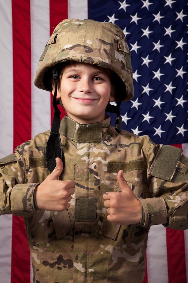 Boy USA soldier is showing thumbs up in front of American flag.