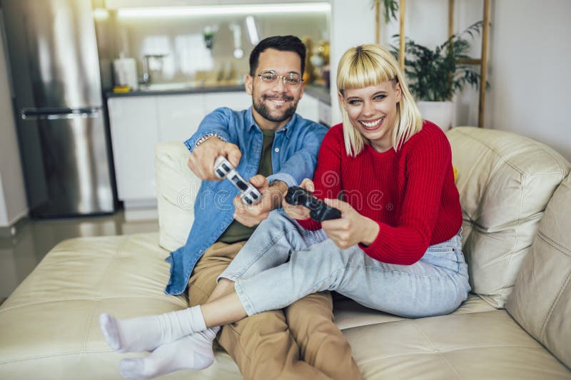 Happy Couple Sitting on the Sofa Playing Video Games, Using Controllers.  Competitive Girlfriend and Boyfriend in Love have Fun Playing in Online  Video Games at Home Together. Close-up Focus on Hands Stock