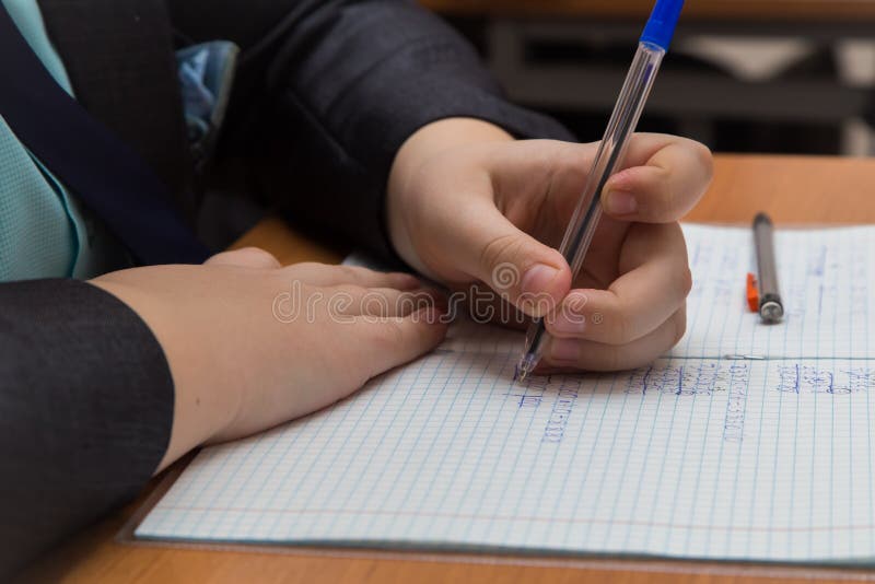 The boys hand with a fountain pen carefully solves a close-up math example. stock photo