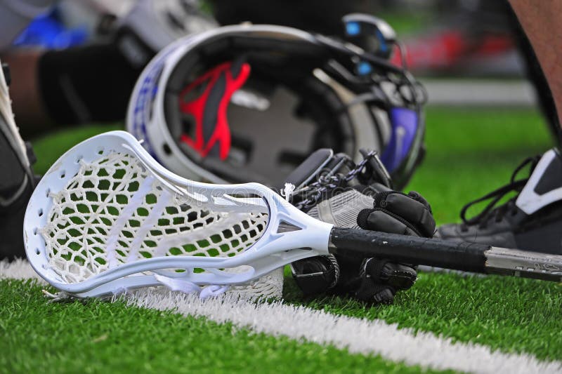 Alta scuola di ragazzi varsity lacrosse bastone testa posa su un campo in erba con i guanti e il casco in background.