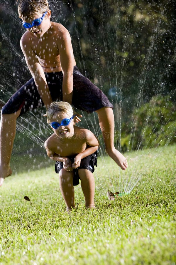 Boys playing leapfrog over lawn sprinkler