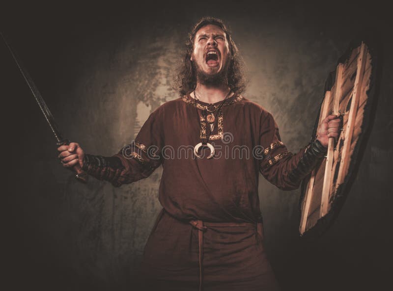 Boze Viking met zwaard in een traditionele strijderskleren, die op een donkere achtergrond stellen royalty-vrije stock afbeeldingen Boze Viking met zwaard in een traditionele strijderskleren, die op een donkere achtergrond stellen royalty-vrije stock afbeeldingen