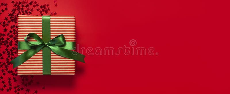 Boîte-cadeau avec le ruban vert et la forme olographe de confettis de scintillement d'étoiles sur la configuration plate rouge de photo stock Boîte-cadeau avec le ruban vert et la forme olographe de confettis de scintillement d'étoiles sur la configuration plate rouge de photo stock