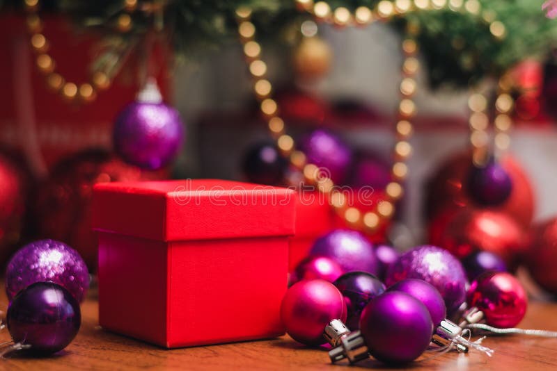Boîte cadeau carrée rouge et boules rouge et violet de Noël sous la veille du Nouvel An avec décorations images libres de droits Boîte cadeau carrée rouge et boules rouge et violet de Noël sous la veille du Nouvel An avec décorations images libres de droits