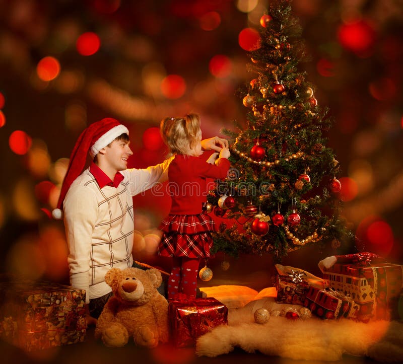 Family decorating Christmas tree. Father in santa hat and kid celebrate Xmas. Family decorating Christmas tree. Father in santa hat and kid celebrate Xmas