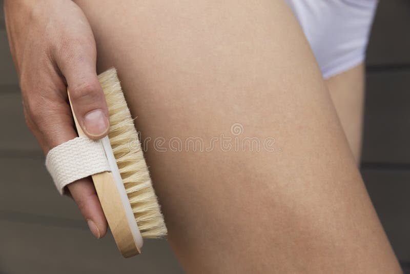 Braccio del ` s della donna che tiene spazzola asciutta alla cima della sua gamba Ossequio delle celluliti fotografia stock Braccio del ` s della donna che tiene spazzola asciutta alla cima della sua gamba Ossequio delle celluliti fotografia stock