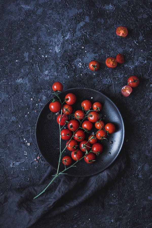 Branch of ripe cherry tomatoes on black plate, top view.