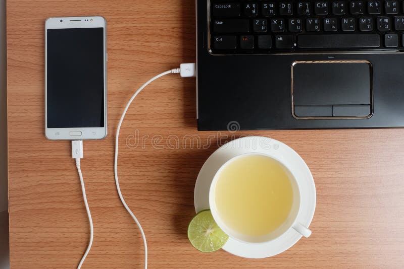 Branchez le chargeur de corde d'USB du téléphone portable avec un ordinateur portable et fraîchement un jus de limette dans une t photo stock Branchez le chargeur de corde d'USB du téléphone portable avec un ordinateur portable et fraîchement un jus de limette dans une t photo stock