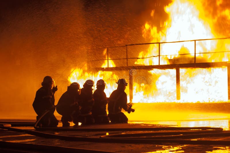 Brandbestrijders die onderaan het branden van structuur tijdens brandbestrijdingsoefening bespuiten