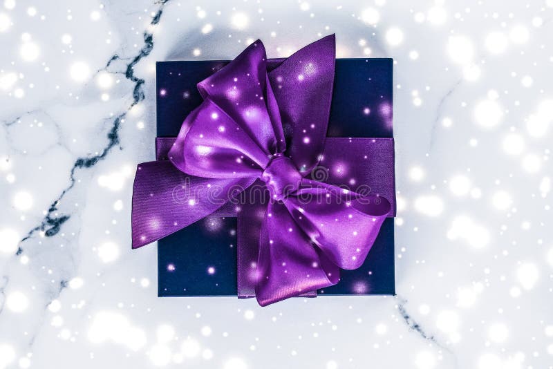 Winter holiday gift box with purple silk bow, snow glitter on marble background as Christmas and New Years presents for luxury