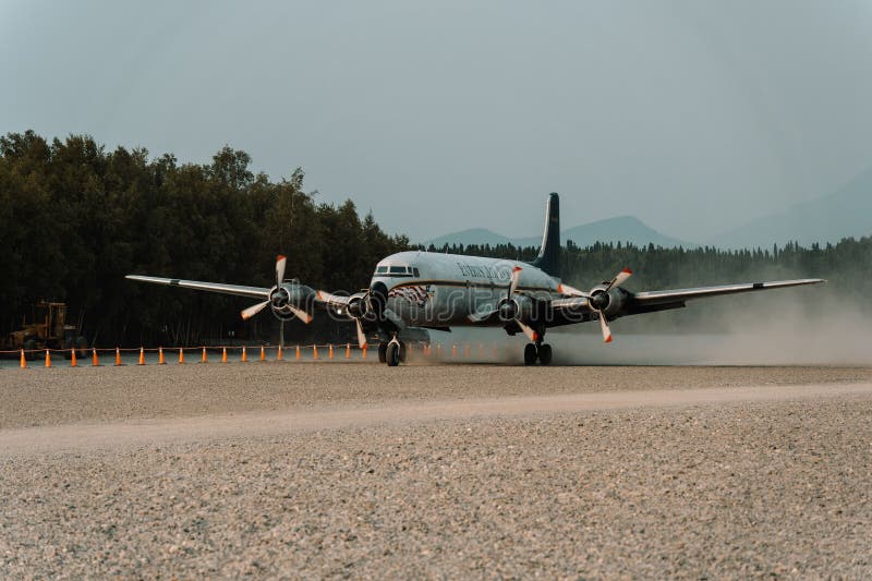 A fuel plane taking off from a runway in the Alaskan wilderness, leaving a trail of white smoke. A fuel plane taking off from a runway in the Alaskan wilderness, leaving a trail of white smoke