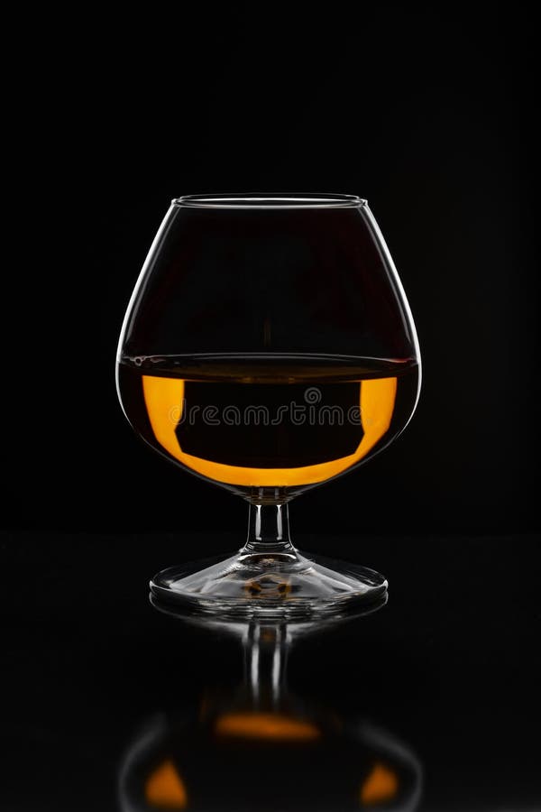Brandy glass filled with half alcoholic drink on a black background in a beautiful light stock photography Brandy glass filled with half alcoholic drink on a black background in a beautiful light stock photography