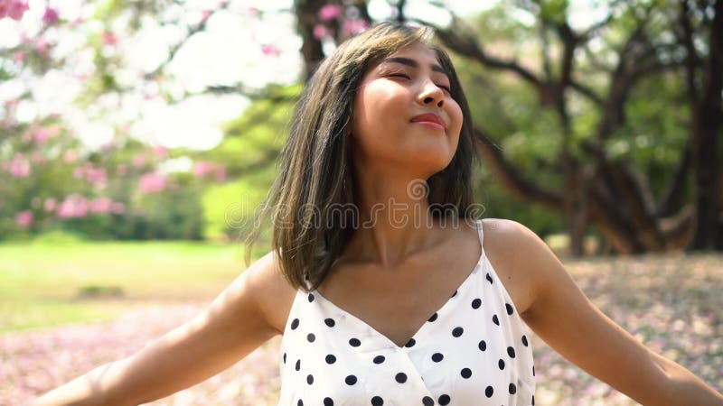 Bras de propagation de jeune femme superbe dans le parc. Fille mignonne dans la danse de robe d'été dans le jardin fleuri clips vidéos