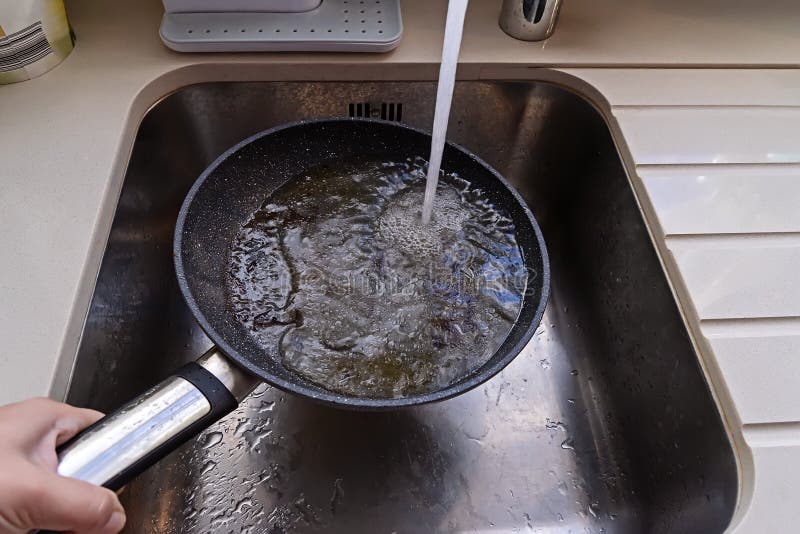 POV of frying pan with non-stick surface and hot oil under water tap flow in sink. Care kitchenware concept. POV of frying pan with non-stick surface and hot oil under water tap flow in sink. Care kitchenware concept