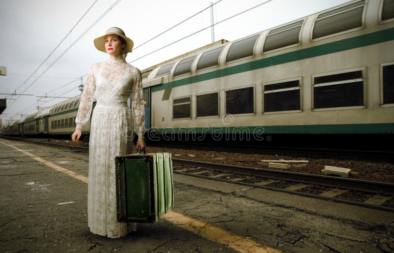 Portrait of a woman in white dress standing on the platform of a train station with an old suitcase in her hand. Portrait of a woman in white dress standing on the platform of a train station with an old suitcase in her hand