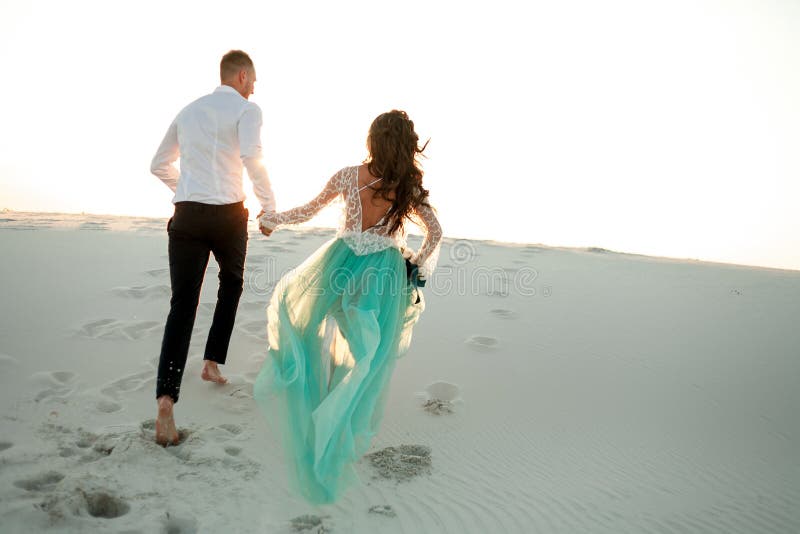 Braut und Bräutigam halten Hände und Lauf auf Sand in der Wüste Rückseitige Ansicht lizenzfreie stockfotografie Braut und Bräutigam halten Hände und Lauf auf Sand in der Wüste Rückseitige Ansicht lizenzfreie stockfotografie