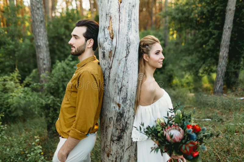 Bride and groom lean on the tree from different sides. Newlyweds are walking in the forest. Artwork,. Bride and groom lean on the tree from different sides. Newlyweds are walking in the forest. Artwork,