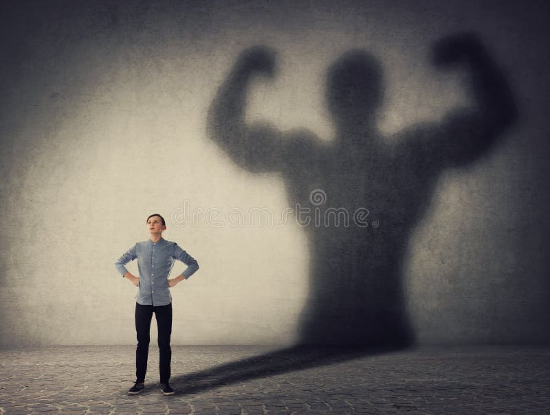 Brave teenager boy facing his fears as a powerful hero. Guy casting a strong muscular bodybuilder shadow, showing big biceps. Self