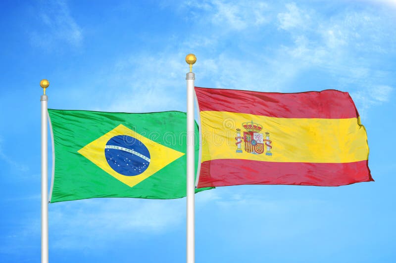 Brazil and Spain Two Flags on Flagpoles and Blue Cloudy Sky Stock Photo