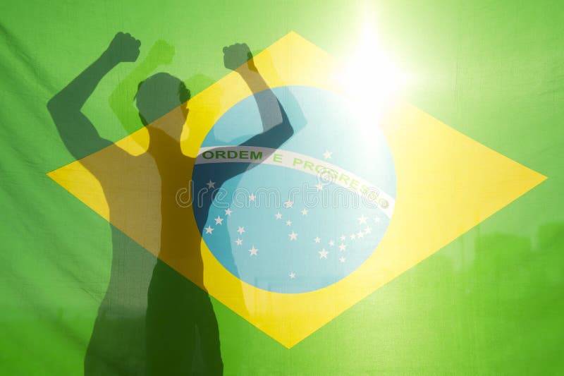 Shadow silhouette of man with arms raised behind Brazilian flag backlit by bright sun. Shadow silhouette of man with arms raised behind Brazilian flag backlit by bright sun