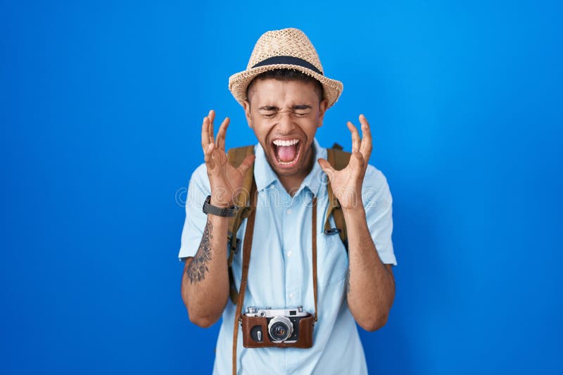 Brazilian young man holding vintage camera celebrating mad and crazy for success with arms raised and closed eyes screaming excited. winner concept. Brazilian young man holding vintage camera celebrating mad and crazy for success with arms raised and closed eyes screaming excited. winner concept