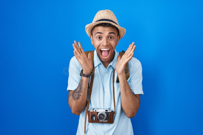 Brazilian young man holding vintage camera celebrating crazy and amazed for success with arms raised and open eyes screaming excited. winner concept. Brazilian young man holding vintage camera celebrating crazy and amazed for success with arms raised and open eyes screaming excited. winner concept