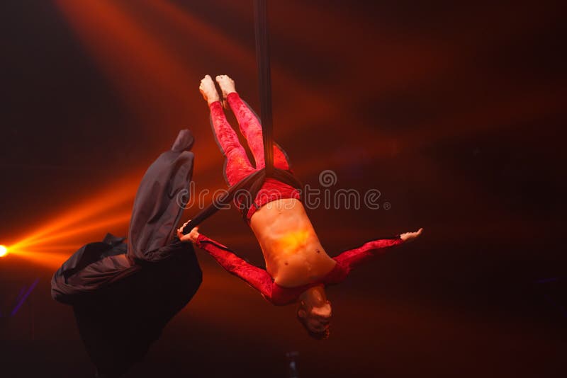 Brazilian strong sexy man do performance on aerial silks in red lights. Sport training gym and lifestyle concept. Black