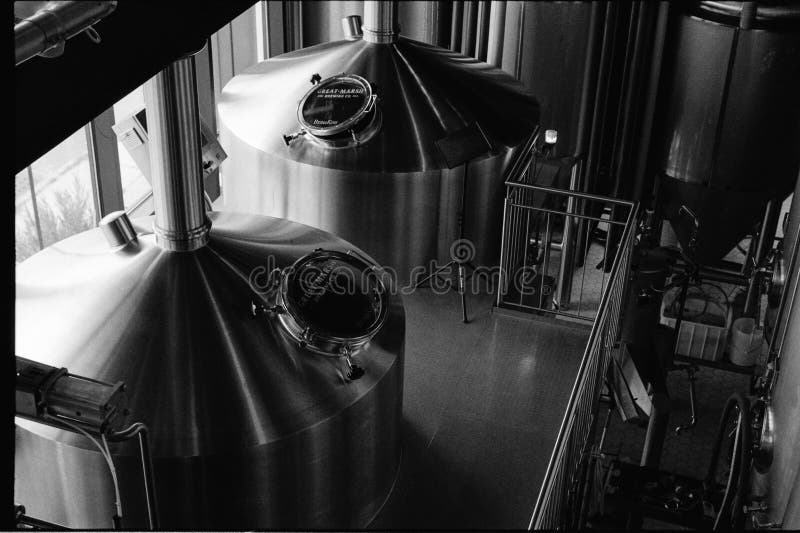 The interior of a brew pub with two metal fermentation tanks visible in front of windows in Essex, Massachusetts. The image was captured on black and white analog film. The interior of a brew pub with two metal fermentation tanks visible in front of windows in Essex, Massachusetts. The image was captured on black and white analog film