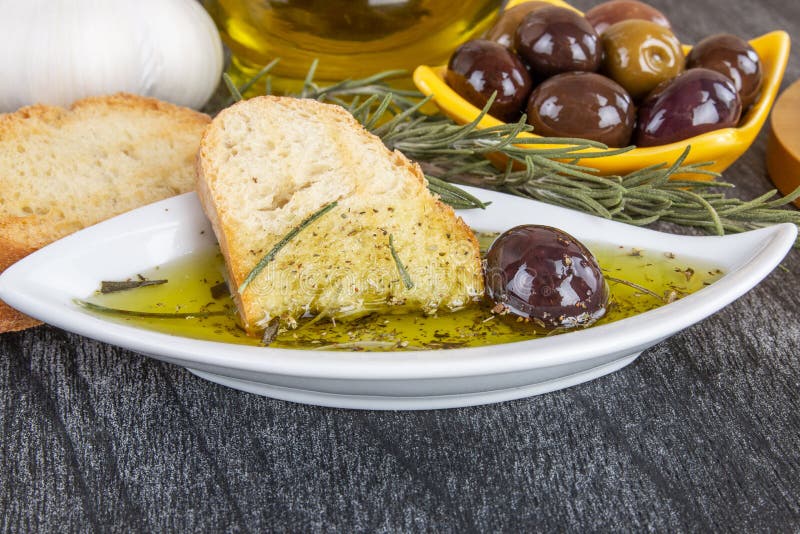 Italian Bread with Oil for Dipping with Herbs & Spices. Olive oil sauce in white bowl & Greek olives on wood background