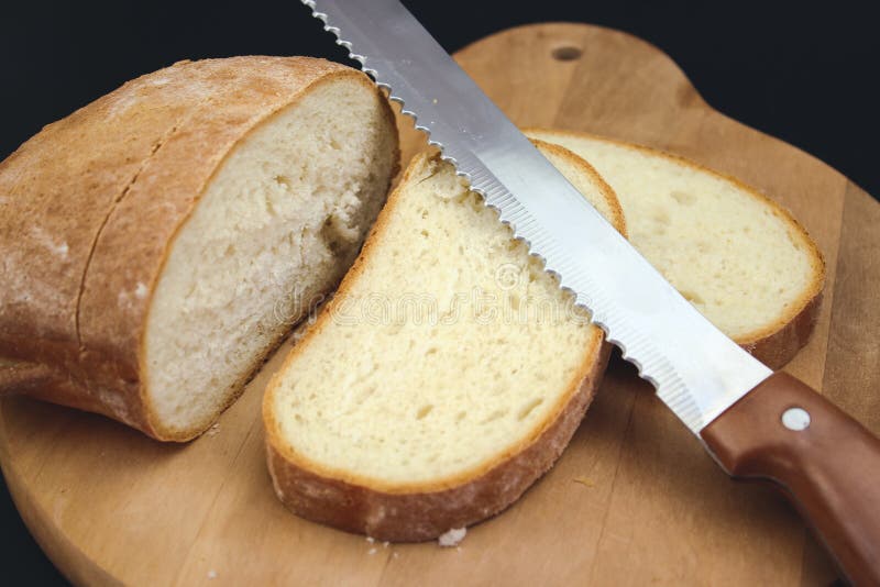 Bread Knife Slicing through a Loaf. Cut Fresh Bread with a Knife Stock