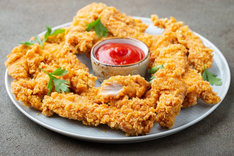 Breaded chicken strips with tomato ketchup on a white plate. Fast food on dark brown background