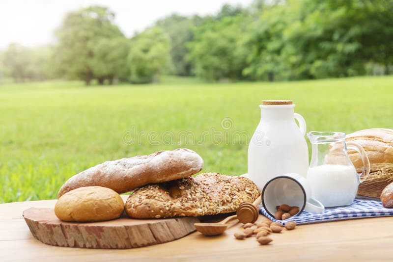 Fresh breads and milk on wood table with blurred green garden background.