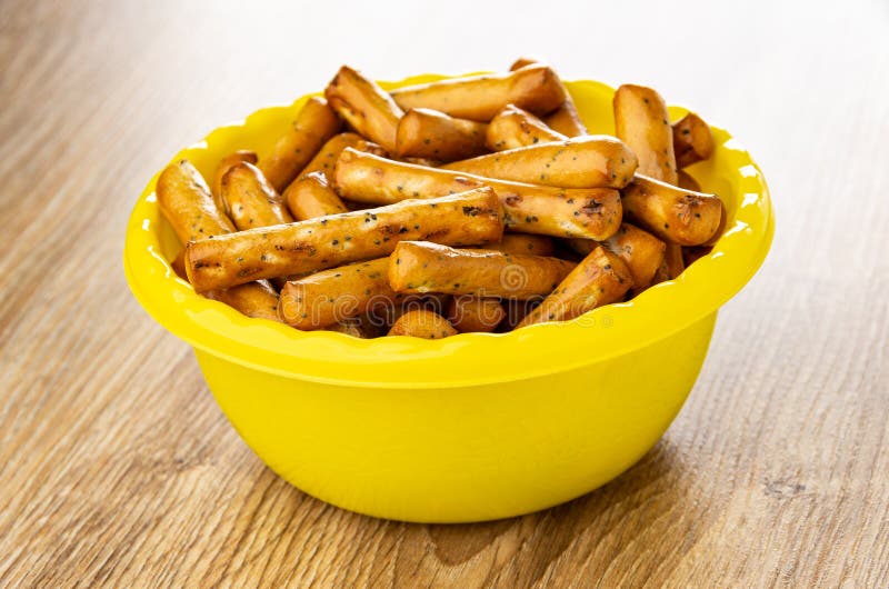 Breadsticks с маком в желтом шаре на деревянном столе. Breadsticks с маком в желтом пластмассовый шаре на коричневом деревянном столе