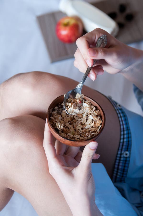 Breakfast in bed, a girl in a blue shirt sitting on a white sheet and Breakfast cereal with milk.