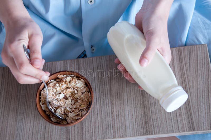 Breakfast in bed, a girl in a blue shirt sitting on a white sheet and Breakfast cereal with milk. Girl holding a bottle of milk, healthy diet