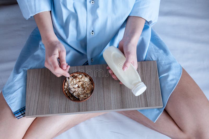 Breakfast in bed, a girl in a blue shirt sitting on a white sheet and Breakfast cereal with milk. Girl holding a bottle of milk, healthy diet