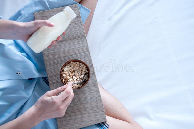 Breakfast in bed, a girl in a blue shirt sitting on a white sheet and Breakfast cereal with milk. Girl holding a tray of food.