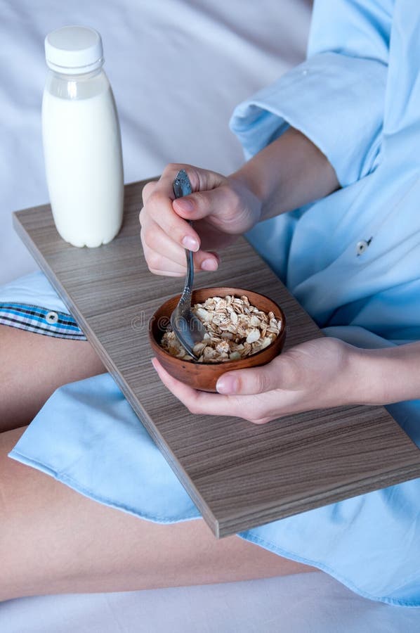 Breakfast in bed, a girl in a blue shirt sitting on a white sheet and Breakfast cereal with milk. Girl holding a tray of food.