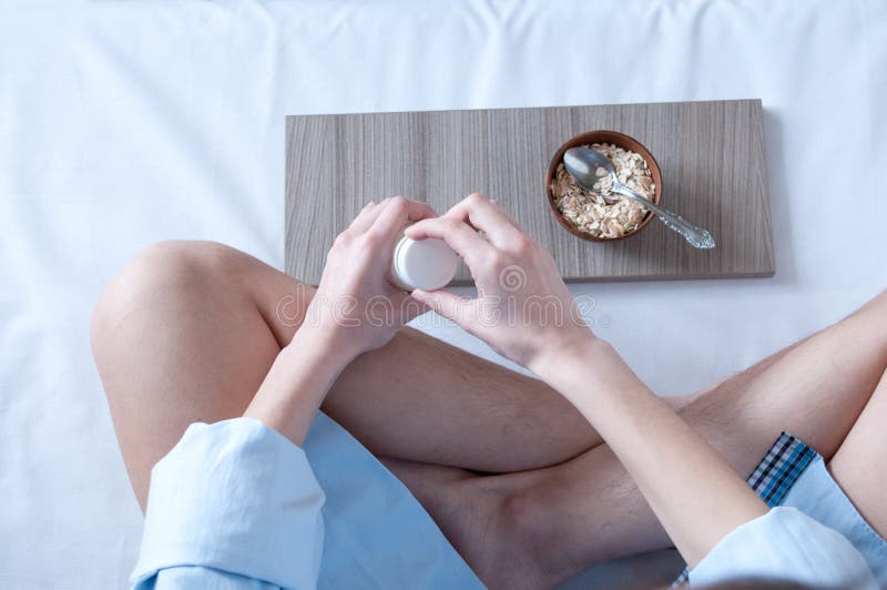 Breakfast in bed, a girl in a blue shirt sitting on a white sheet and Breakfast cereal with milk. The girl opens a bottle of milk, healthy diet