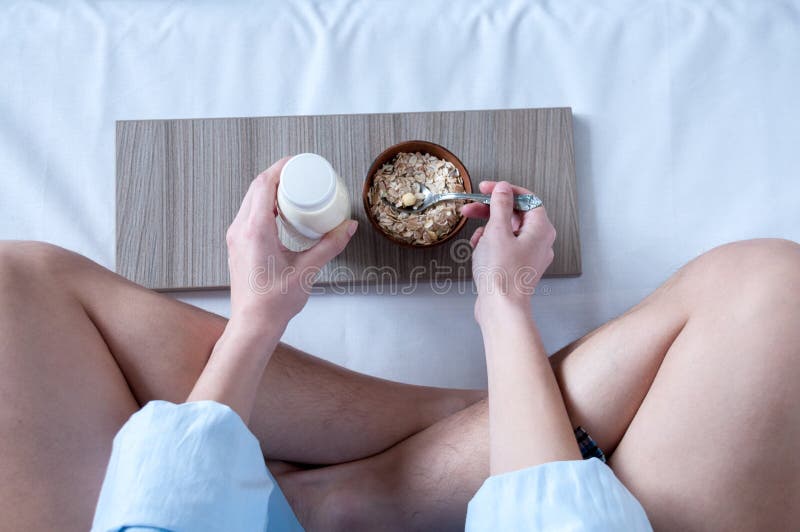 Breakfast in bed, a girl in a blue shirt sitting on a white sheet and Breakfast cereal with milk, healthy diet