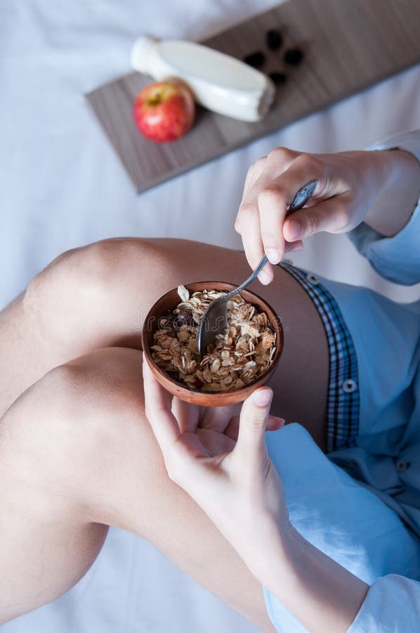 Breakfast in bed, a girl in a blue shirt sitting on a white sheet and Breakfast cereal with milk, healthy diet