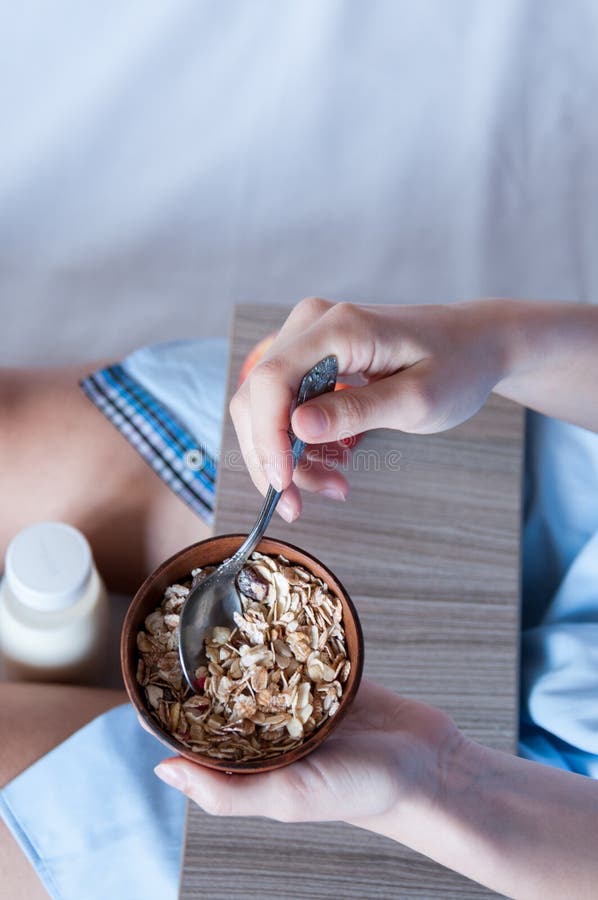 Breakfast in bed, a girl in a blue shirt sitting on a white sheet and Breakfast cereal with milk.