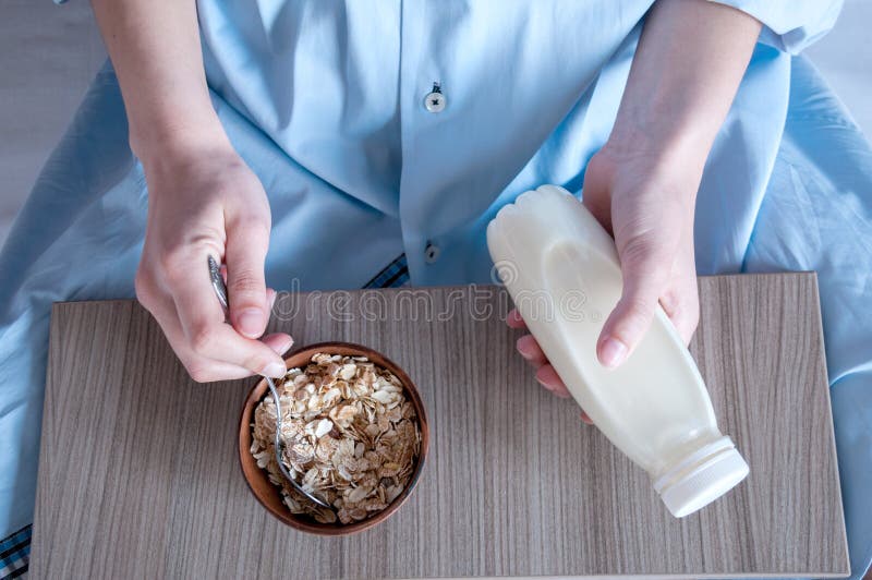 Breakfast in bed, a girl in a blue shirt sitting on a white sheet and Breakfast cereal with milk. Girl holding a bottle of milk.