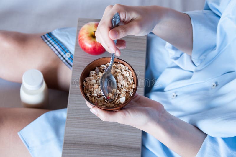 Breakfast in bed, a girl in a blue shirt sitting on a white sheet and Breakfast cereal with milk. Girl holding a Cup of porridge, healthy diet