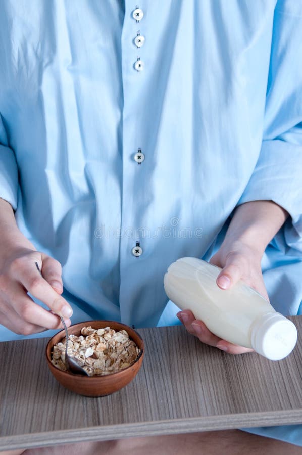 Breakfast in bed, a girl in a blue shirt sitting on a white sheet and Breakfast cereal with milk. Girl holding a tray of food.