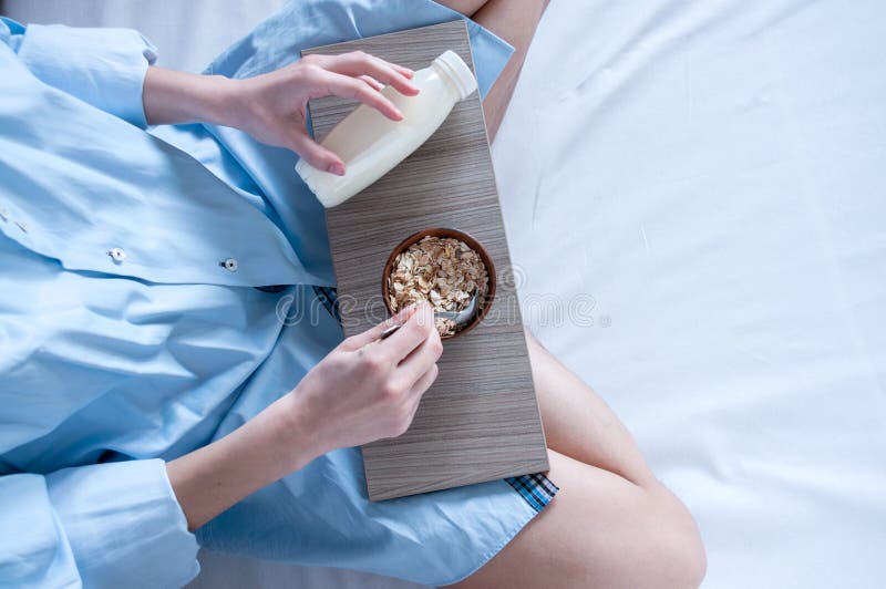 Breakfast in bed, a girl in a blue shirt sitting on a white sheet and Breakfast cereal with milk. Girl holding a tray of food, healthy diet