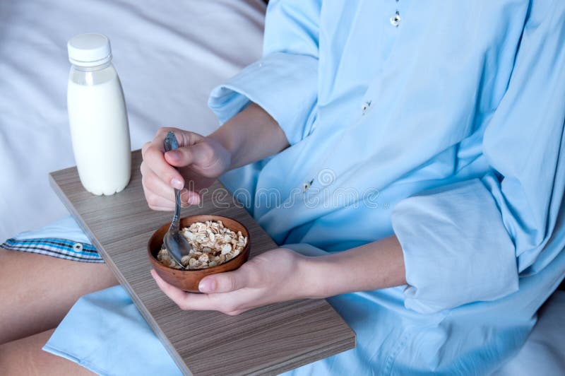 Breakfast in bed, a girl in a blue shirt sitting on a white sheet and Breakfast cereal with milk. Girl holding a tray of food, healthy diet