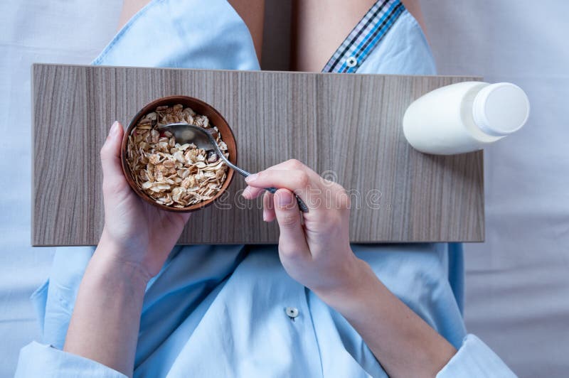 Breakfast in bed, a girl in a blue shirt sitting on a white sheet and Breakfast cereal with milk. Girl holding a tray of food, healthy diet