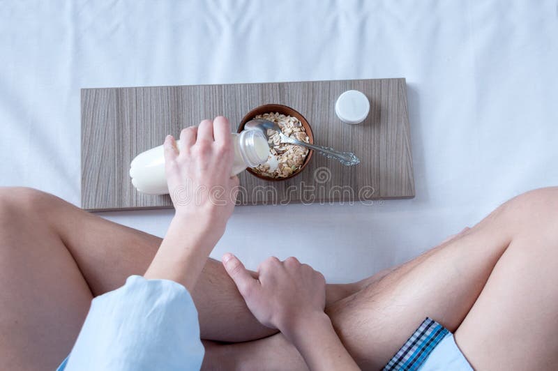 Breakfast in bed, a girl in a blue shirt sitting on a white sheet and Breakfast cereal with milk. The girl pours milk from the bottle into cereal, healthy diet